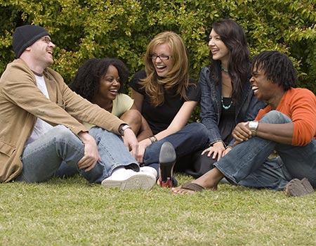 five college students sitting on the grass and smiling